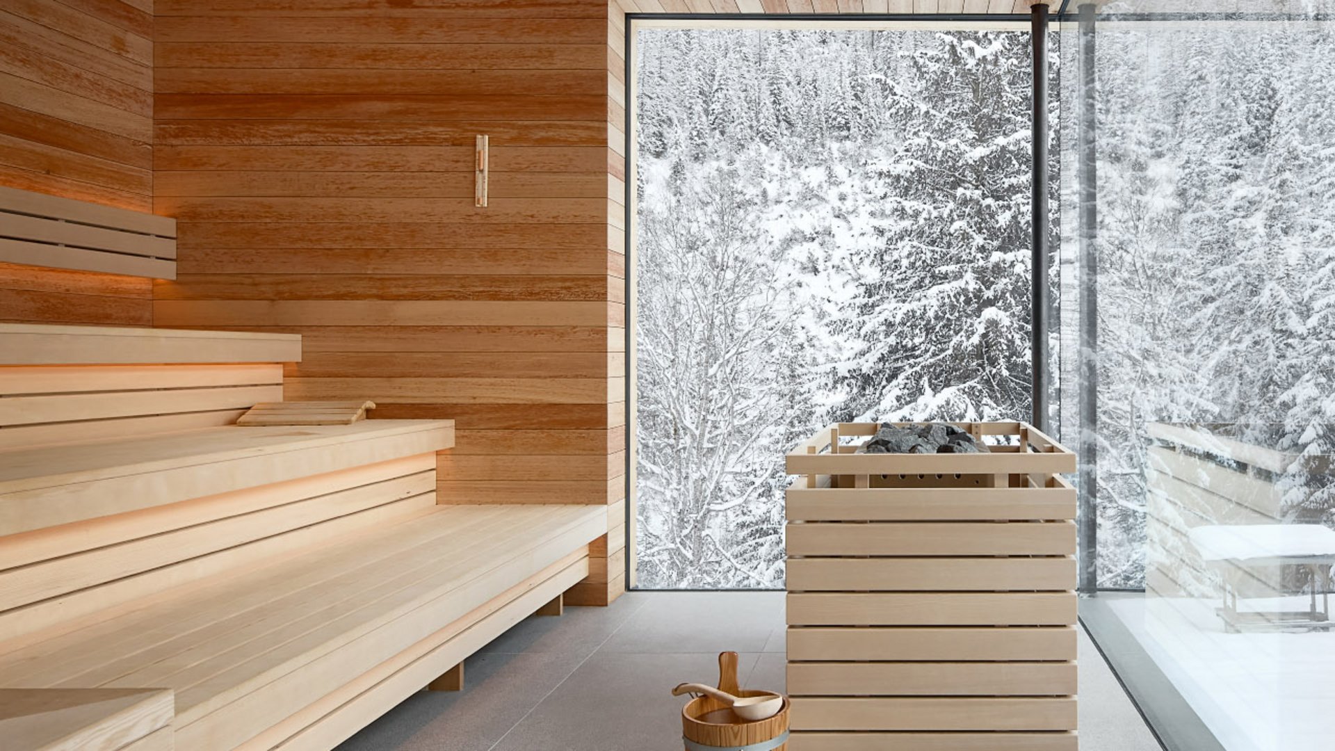 Gemütliche Sauna mit großer Glasfront im Hotel Bella Vista, die den Blick auf die schneebedeckte Waldlandschaft freigibt und eine Atmosphäre der Ruhe schafft.